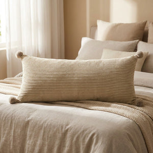 Coussin long en velours côtelé beige sur un lit près d'une fenêtre lumineuse