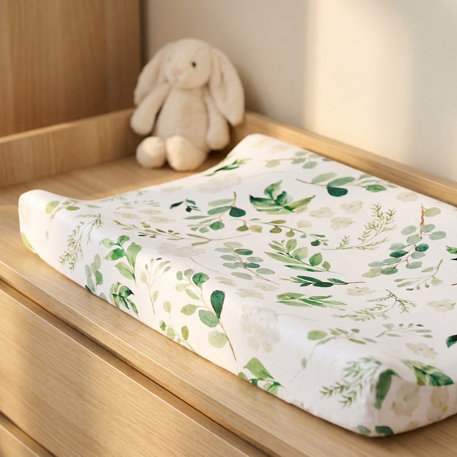 Housse de matelas à langer motif feuillage avec une peluche lapin dans une chambre lumineuse