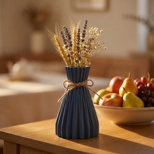 Vase origami plissé bleu foncé avec des fleurs séchées sur un buffet en bois