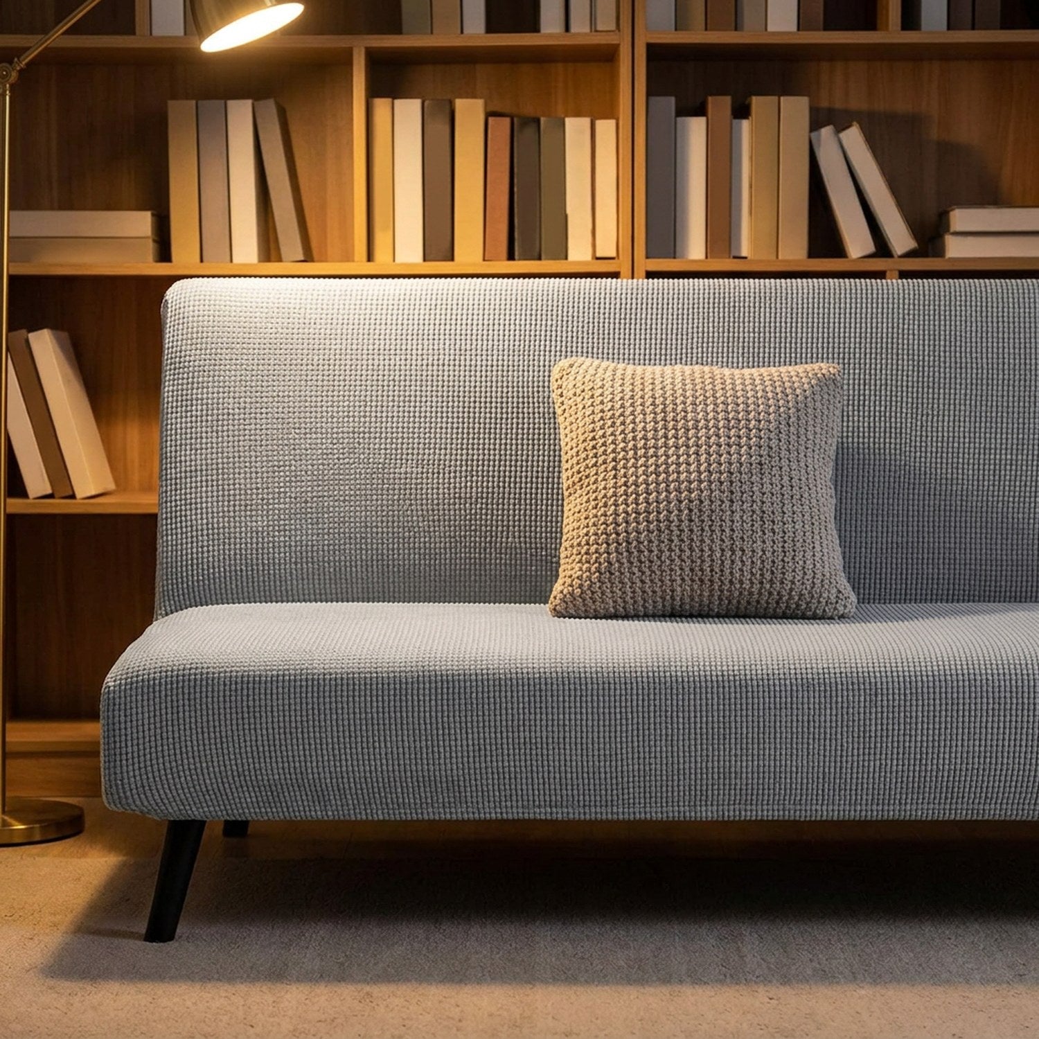 Housse de canapé lit futon grise devant une bibliothèque en bois avec coussin beige
