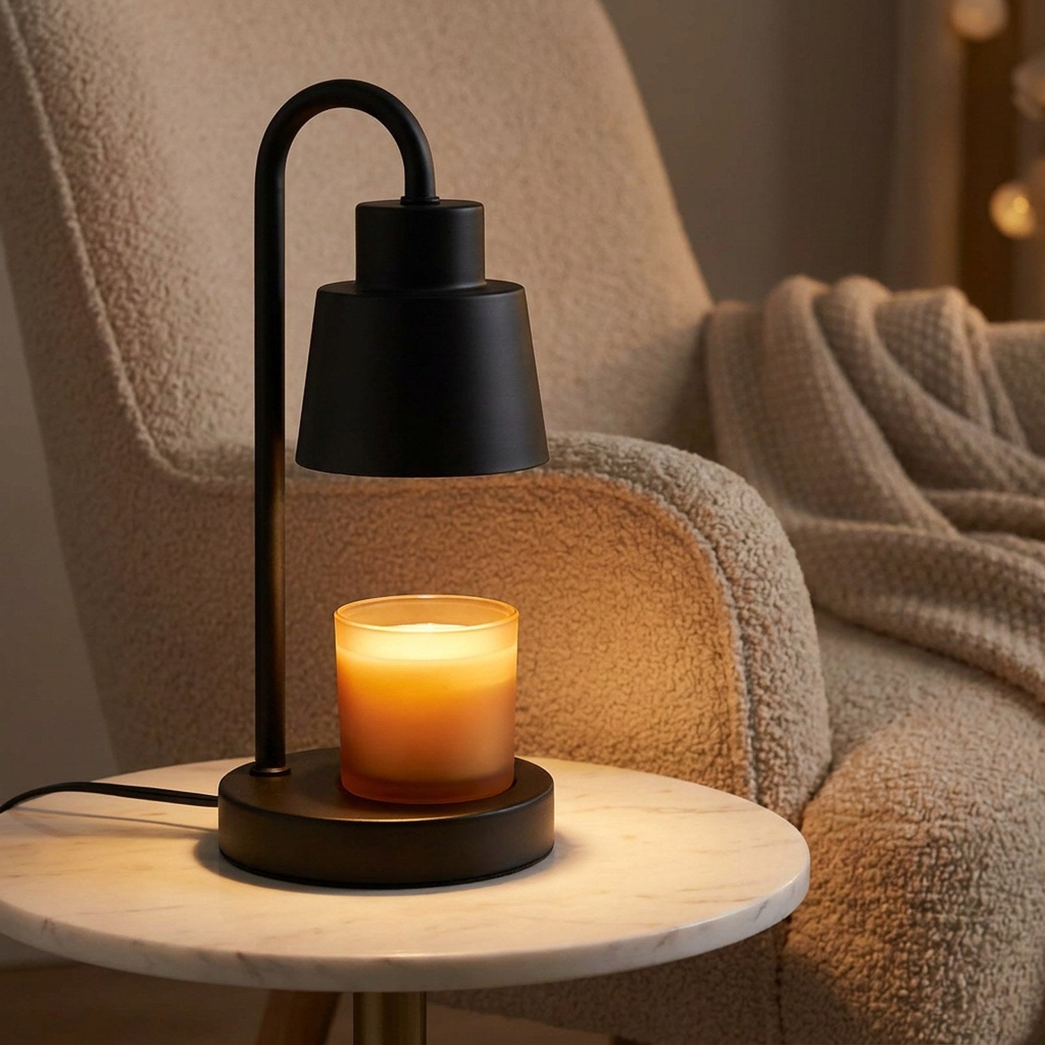 Lampe chauffe-bougie noire sur une table d'appoint en marbre à côté d'un fauteuil cocooning