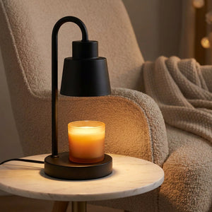 Lampe chauffe-bougie noire sur une table d'appoint en marbre à côté d'un fauteuil cocooning