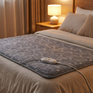 Couverture chauffante à carreaux gris étalée sur un lit avec sa commande et une lampe de chevet