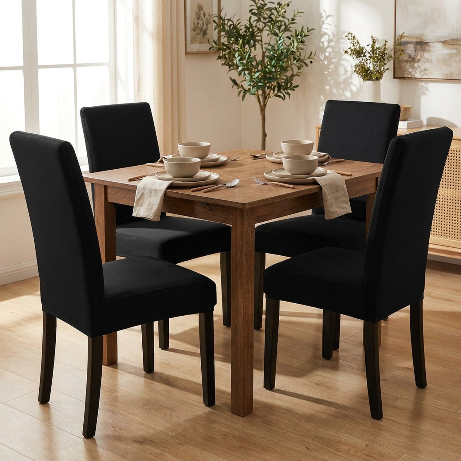 Salle à manger avec quatre chaises habillées de housses noires autour d'une table en bois