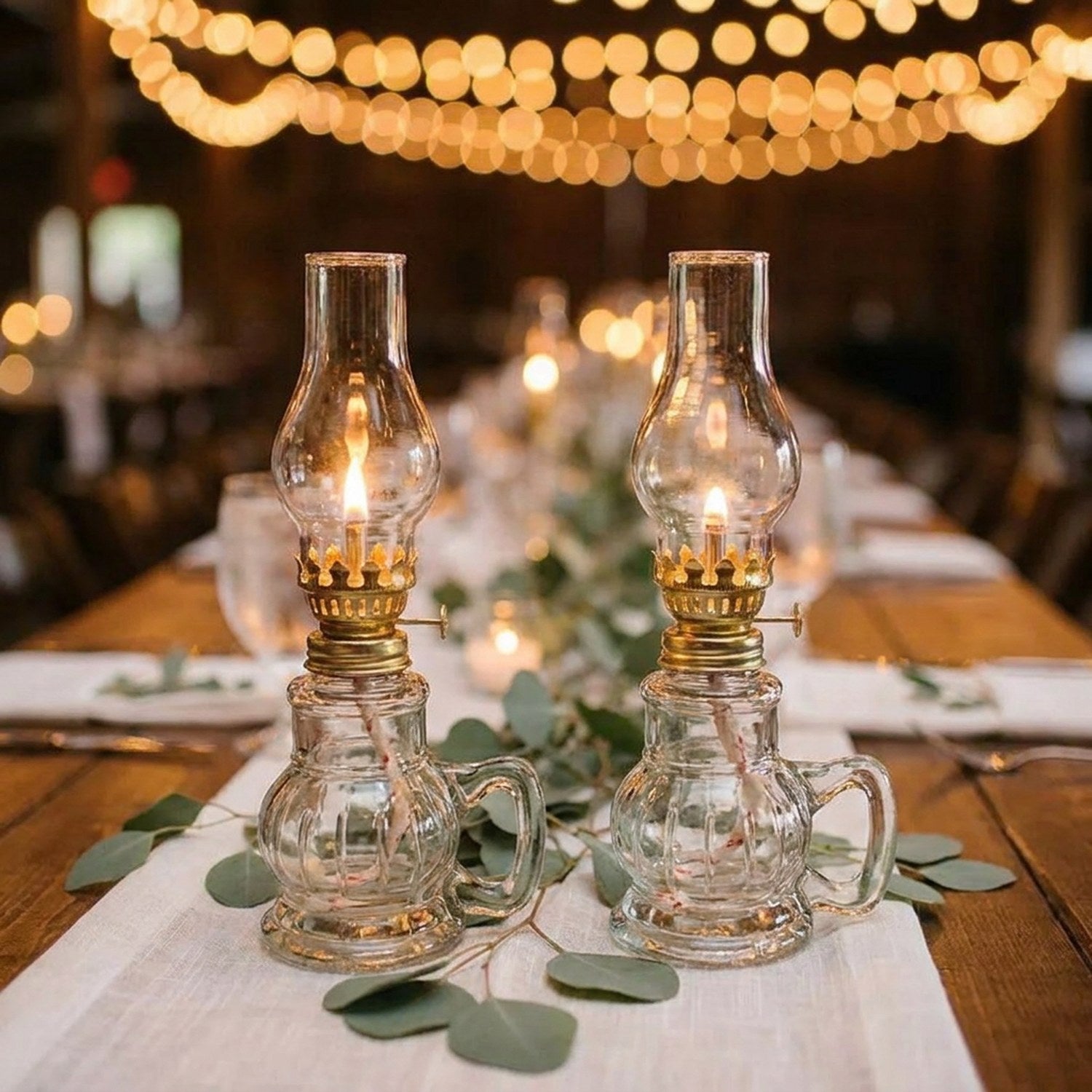 Deux lampes à pétrole allumées sur une table de mariage décorée de verdure