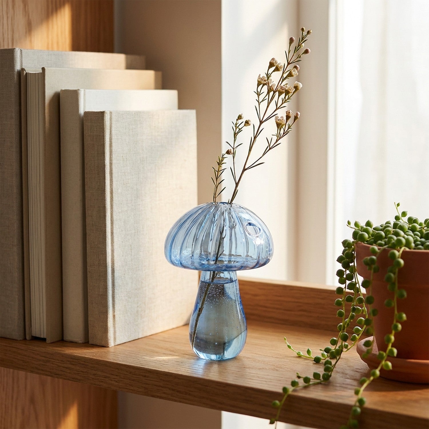 Vase champignon en verre bleu sur étagère avec livres et plante