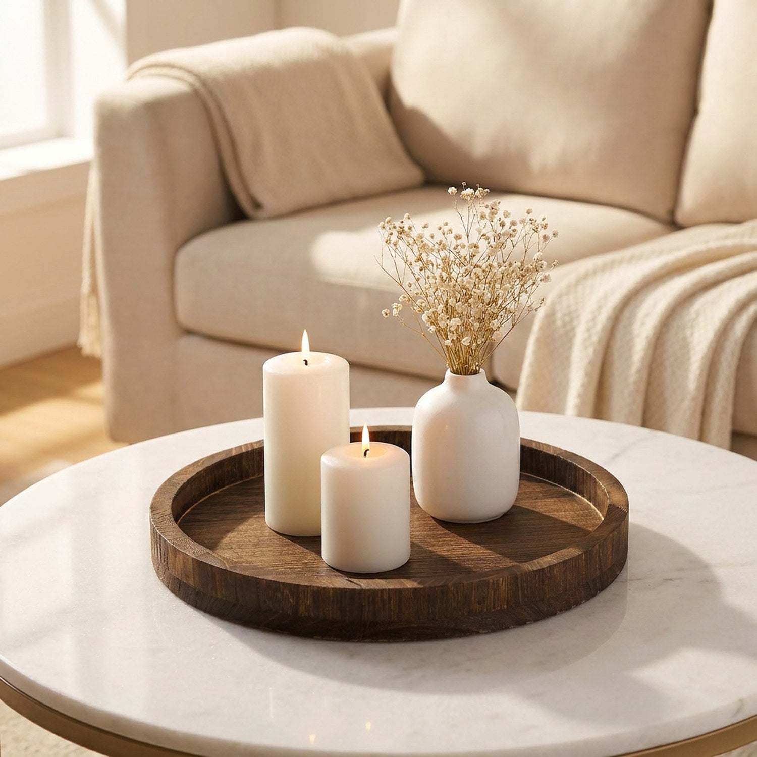 Plateau rond en bois marron sur une table basse en marbre avec bougies et fleurs séchées dans un salon