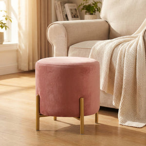 Pouf rond en velours rose utilisé comme repose pieds près d'un fauteuil