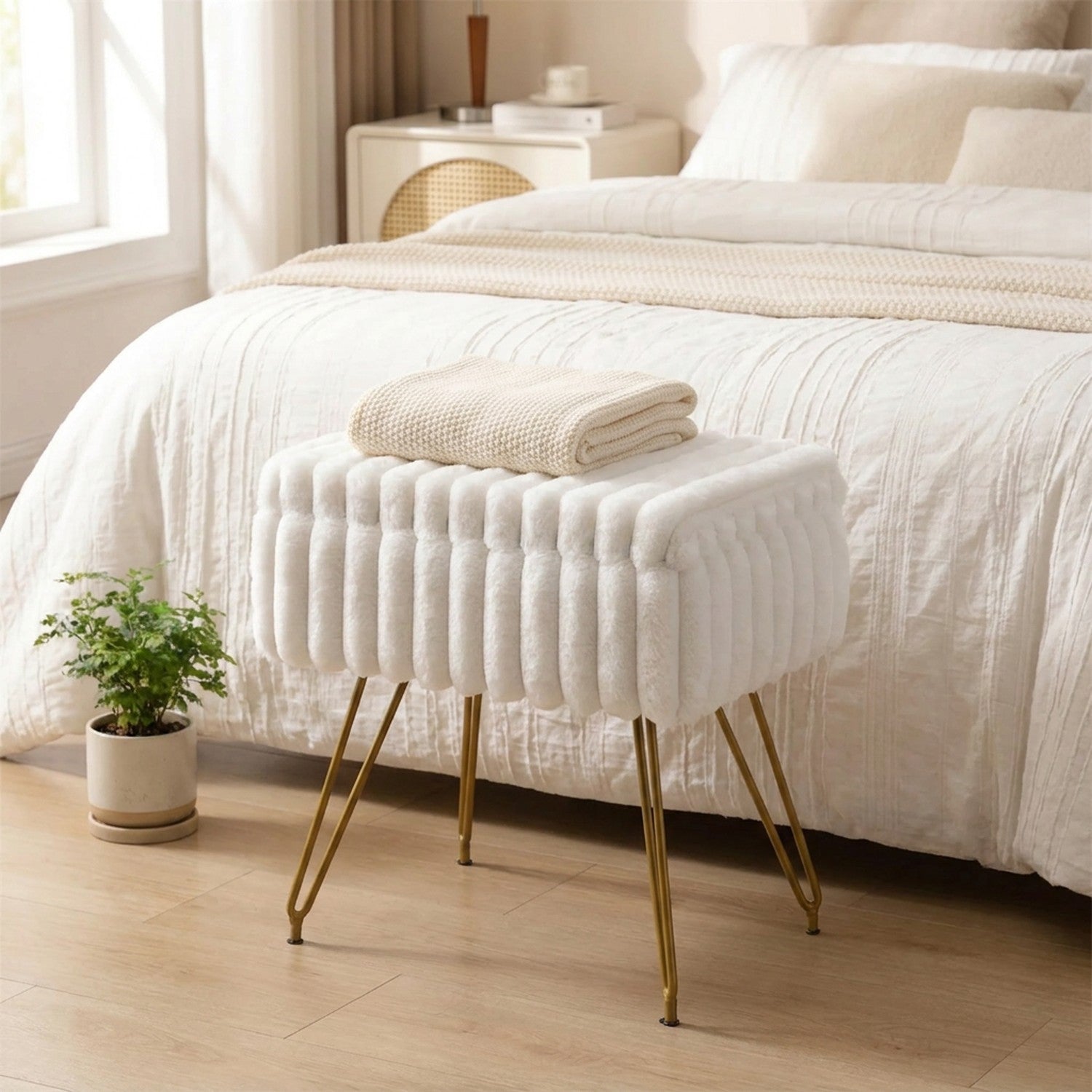 Tabouret coiffeuse en fausse fourrure blanche au pied d'un lit avec un plaid beige