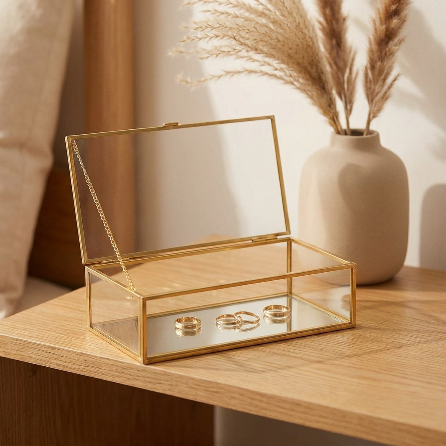 Boîte à bijoux en verre ouverte sur une table en bois avec pampa et bagues