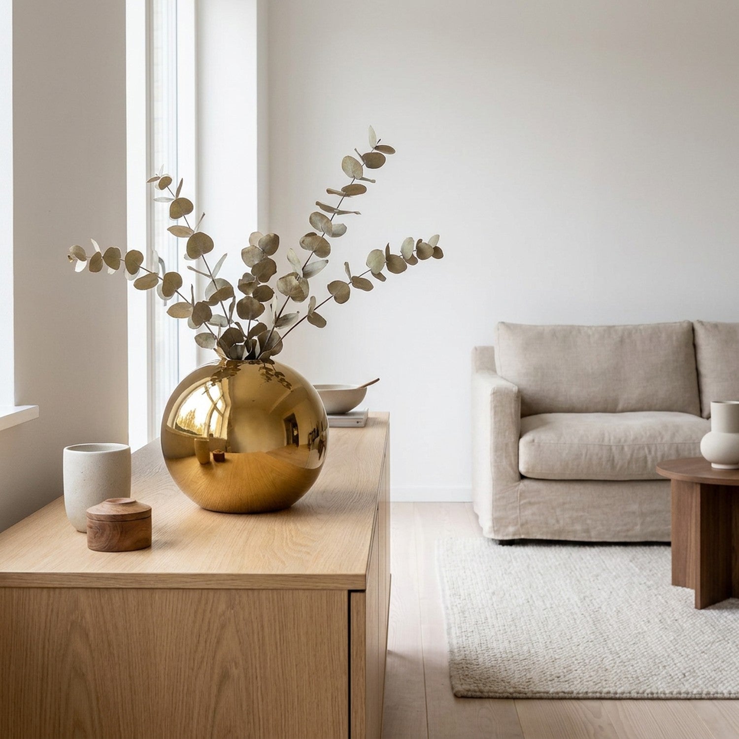 Vase boule doré moyen sur un buffet scandinave avec des branches d'eucalyptus séchées