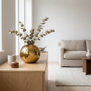 Vase boule doré moyen sur un buffet scandinave avec des branches d'eucalyptus séchées