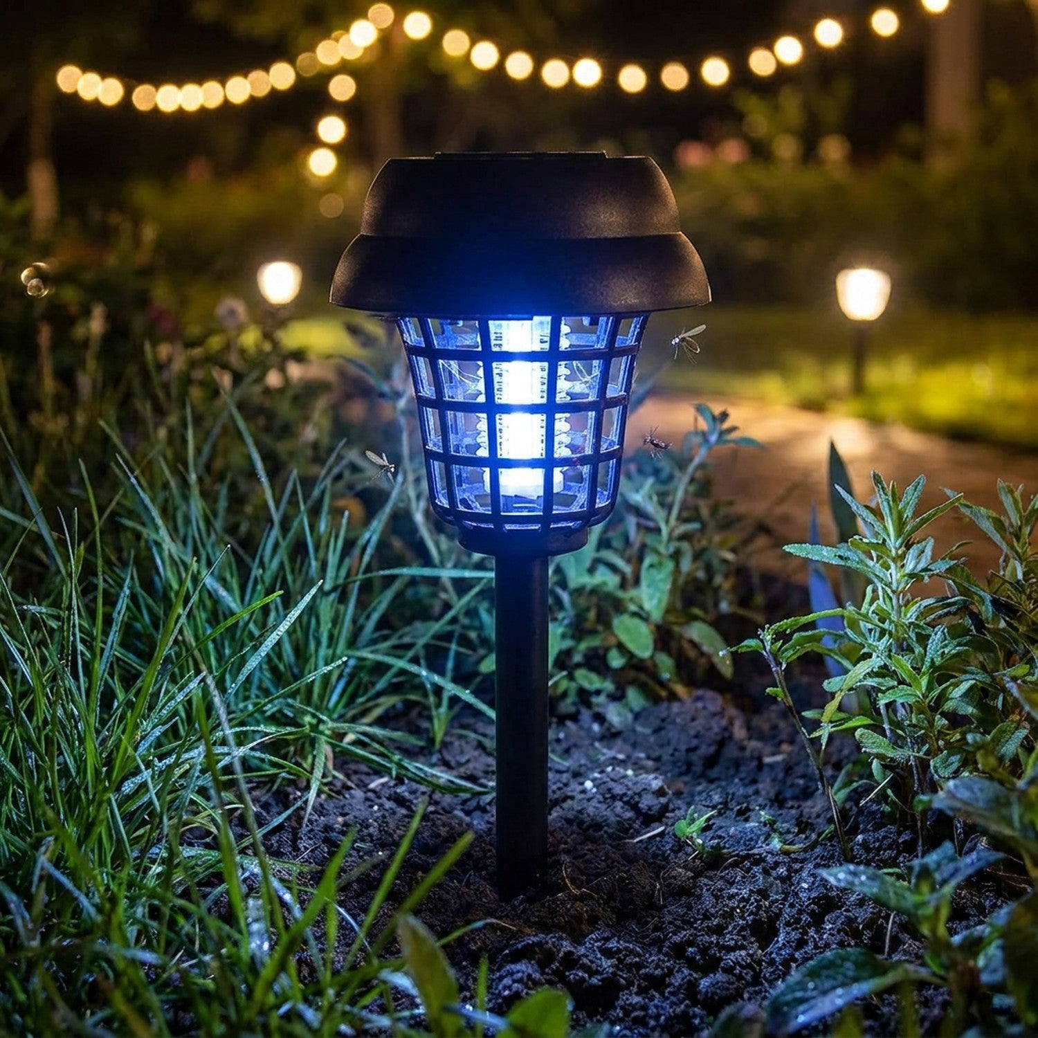 Lampe solaire anti-moustiques plantée dans la terre au milieu d'herbes et plantes nocturnes