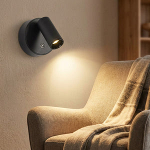 Applique murale LED noire éclairant un fauteuil de lecture cosy avec plaid