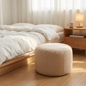Pouf beige posé au sol près d'un lit dans une chambre lumineuse