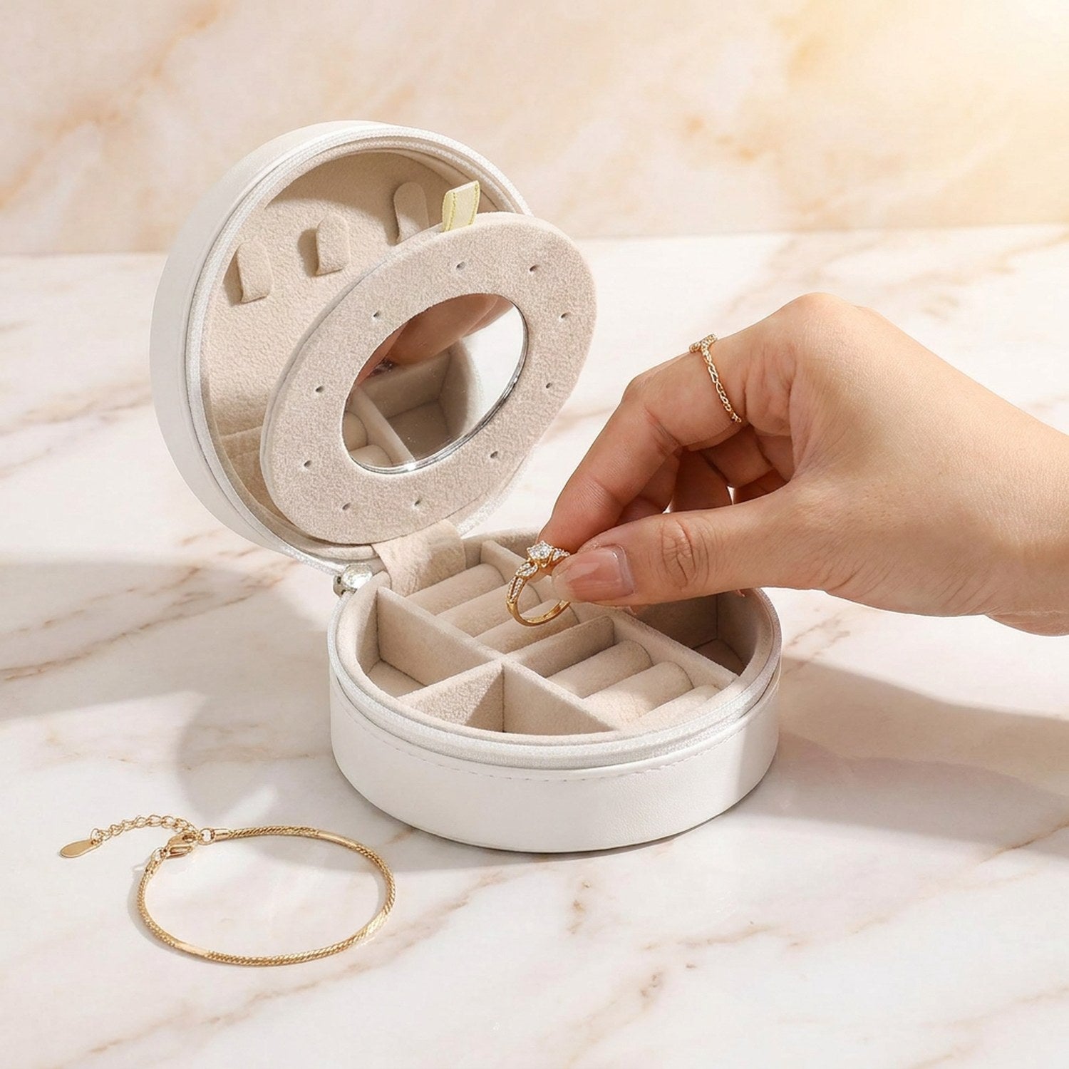 Coffret à bijoux de voyage blanc ouvert sur marbre avec main posant une bague