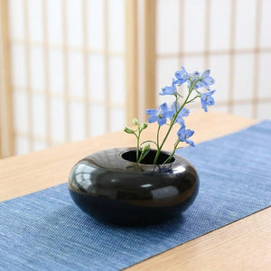 Vase céramique noir brillant sur chemin de table bleu avec fleurs bleues ikebana