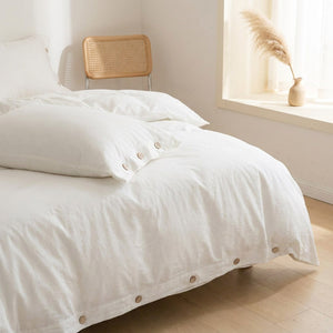 Détail de la housse de couette blanche avec taie boutonnée et chaise en rotin