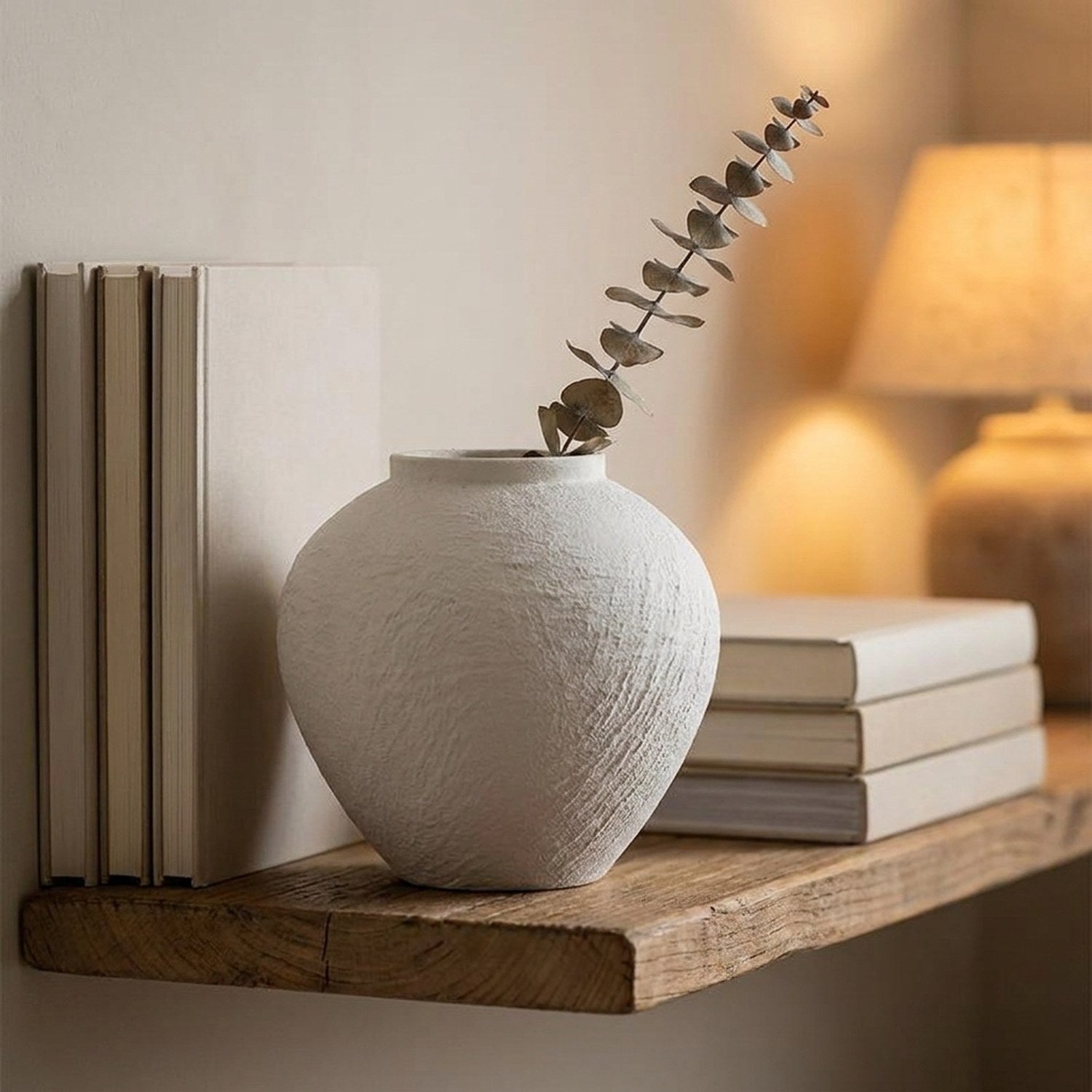 Vase en céramique blanche avec une branche d'eucalyptus sur une étagère en bois