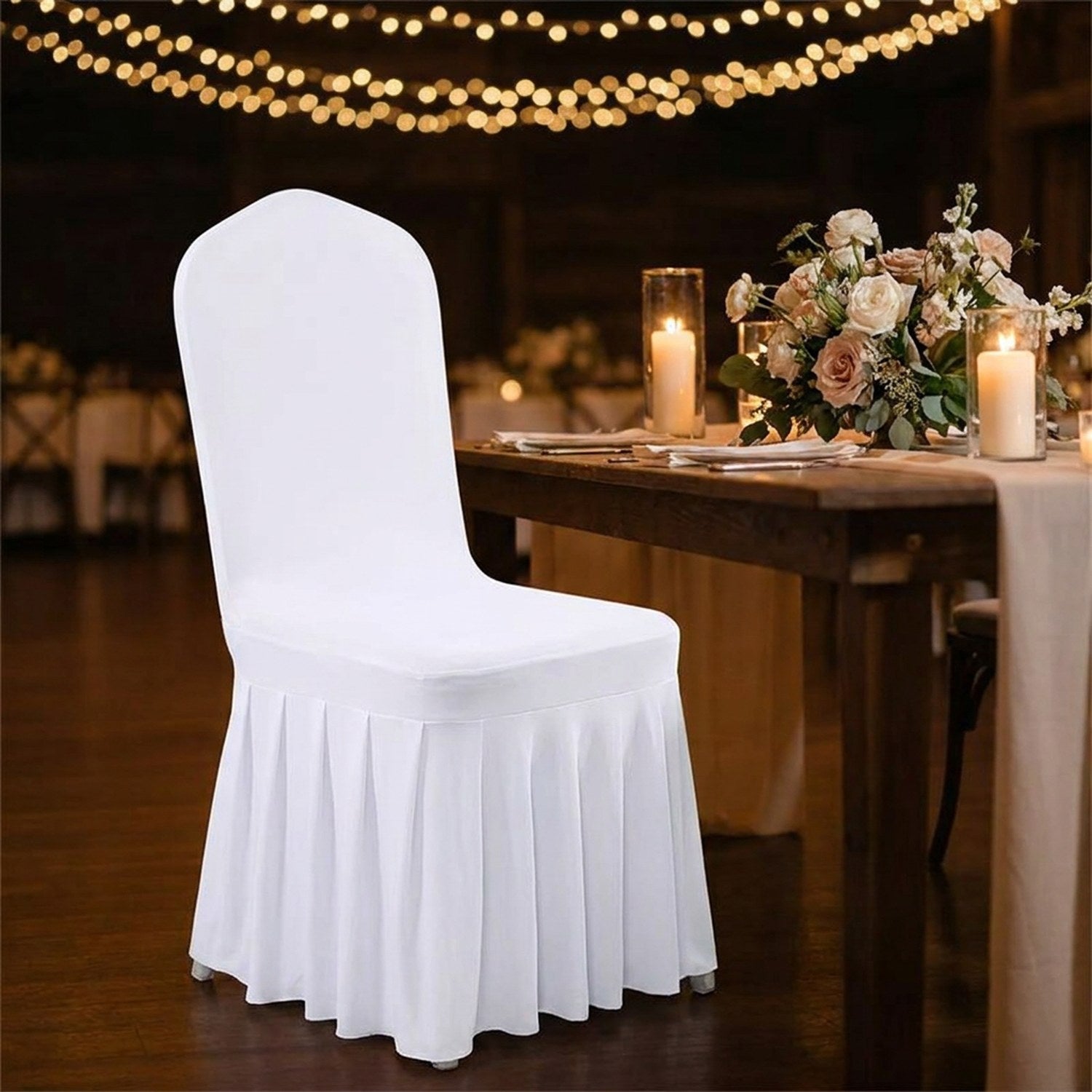 Chaise blanche à jupe plissée près d'une table de réception éclairée aux bougies
