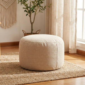 Pouf beige dans un coin salon bohème près d'une fenêtre avec voilage
