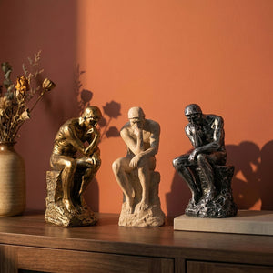 Trois statues de penseur en résine beige dorée et argentée sur console en bois terracotta