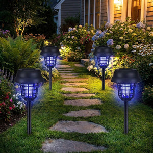 Quatre lampes solaires anti-moustiques UV le long d'un chemin de pierres dans un jardin fleuri la nuit