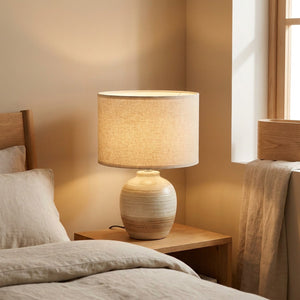 Abat-jour cylindrique en lin naturel 30cm posé sur une lampe de table de chevet allumée dans une chambre cosy