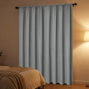 Rideau occultant gris entièrement fermé le soir dans une chambre avec lampe de chevet