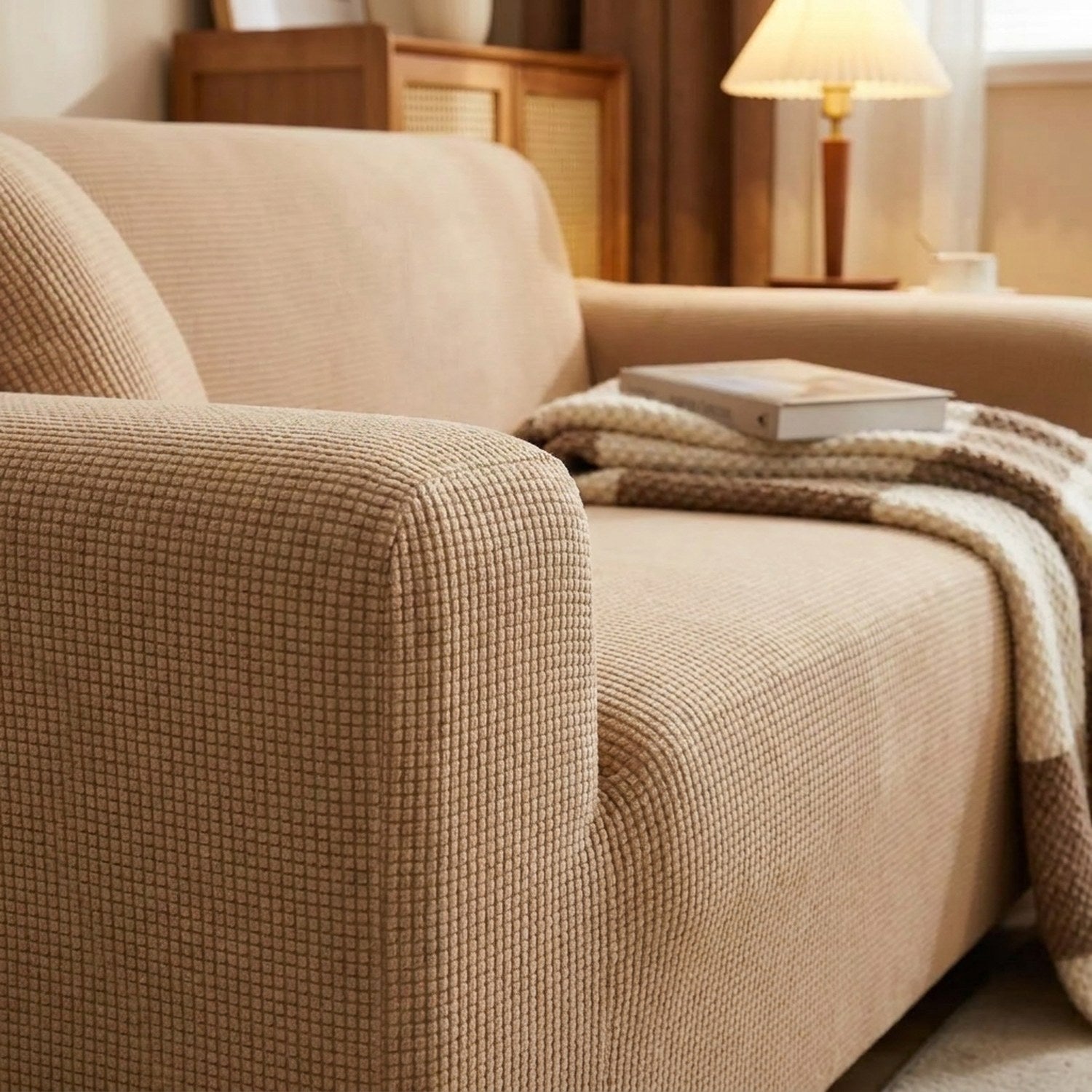 Détail du tissu jacquard de la housse de canapé beige sur un accoudoir avec plaid