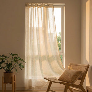 Voilage tulle beige qui ondule doucement devant une fenêtre au coucher du soleil