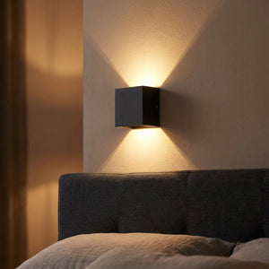 Applique murale LED noire allumée au dessus d'une tête de lit dans une chambre cosy