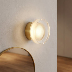 Applique murale LED dorée au verre strié dans une entrée près d'un miroir rond