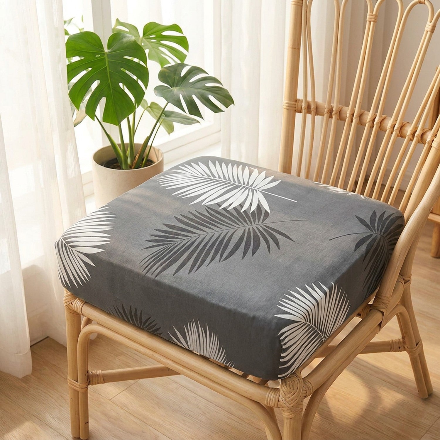 Housse de coussin grise à feuillage sur un fauteuil en rotin près d une fenêtre