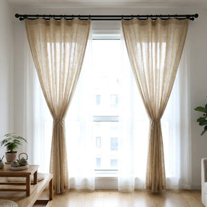 Salon lumineux avec rideaux en lin beige noués sur le côté d'une grande fenêtre