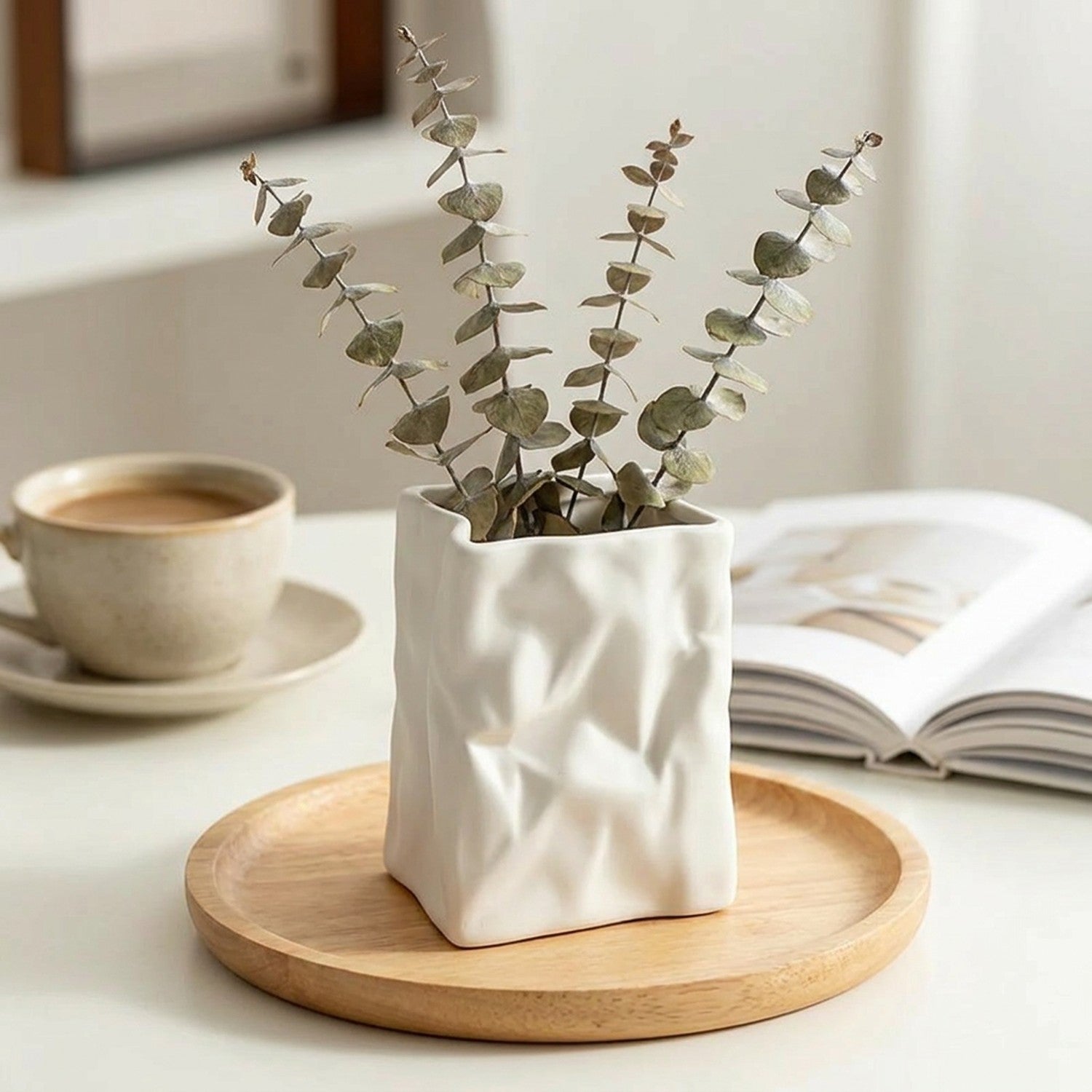 Vase design froissé blanc avec eucalyptus sur plateau bois sur un bureau avec café et livre