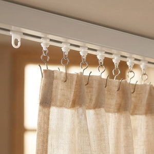 Rangée de crochets et anneaux coulissants tenant un rideau en lin beige sur un rail de plafond