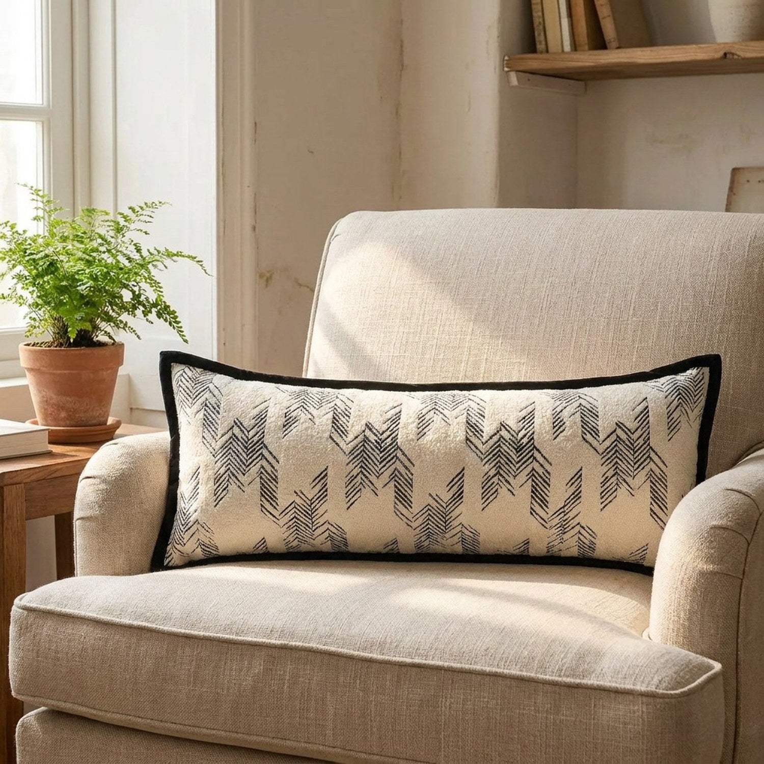 Traversin à motif chevrons noirs sur un fauteuil en lin beige près d'une fenêtre