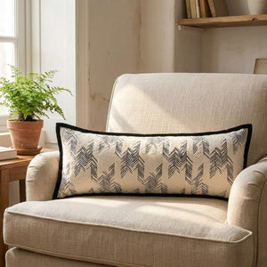Traversin à motif chevrons noirs sur un fauteuil en lin beige près d'une fenêtre
