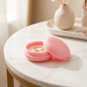 Boîte macaron rose ouverte avec bague sur table en marbre