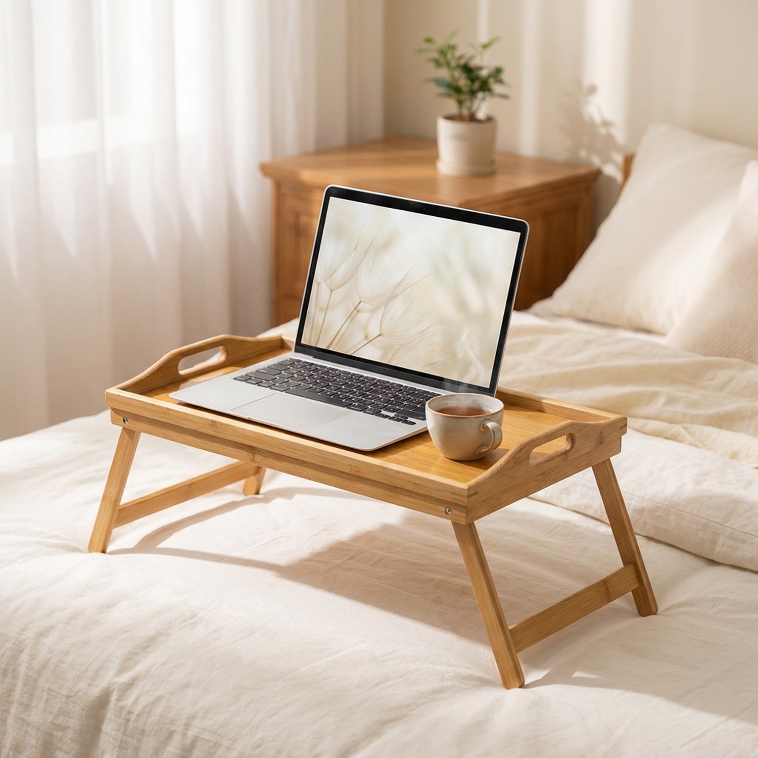 Plateau de lit en bambou pliant posé sur un lit avec literie crème et ordinateur portable ouvert