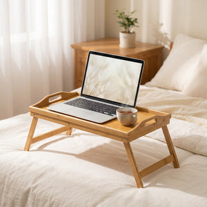 Plateau de lit en bambou pliant posé sur un lit avec literie crème et ordinateur portable ouvert