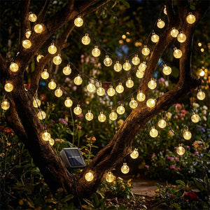 Guirlande lumineuse solaire à globes dorés sur arbre de jardin la nuit