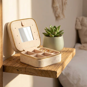 Boîte à bijoux de voyage en velours posée ouverte sur étagère en bois avec plante verte