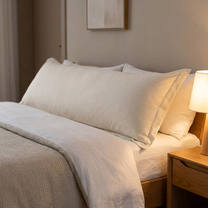 Taie de traversin beige installée sur un lit dans une chambre moderne avec table de chevet