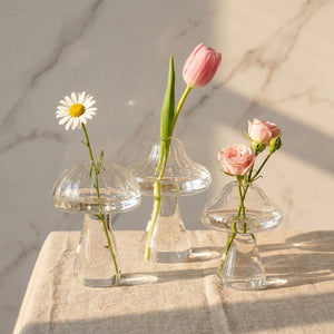 Trois vases champignon verre transparent avec fleurs fraîches sur marbre, vue groupée