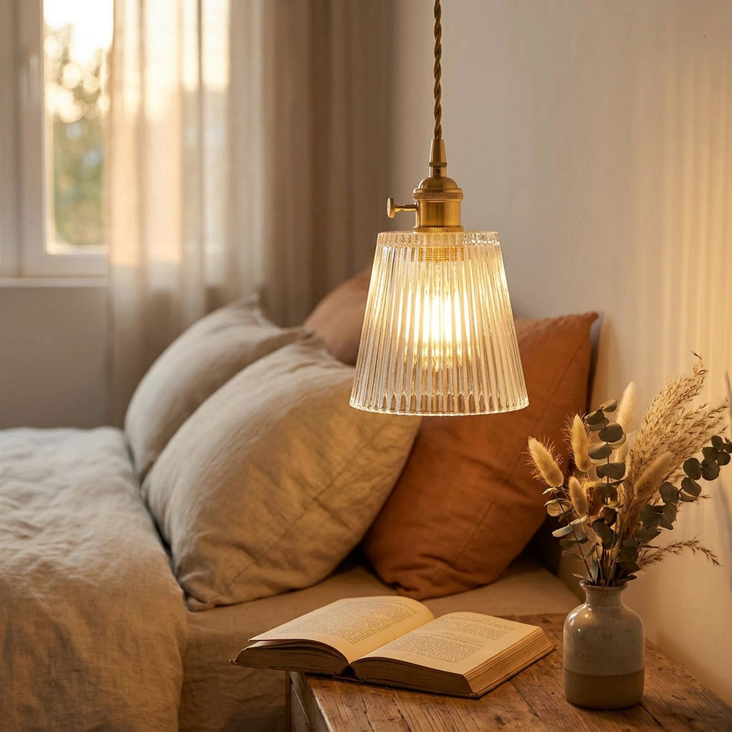 Suspension en verre strié transparent laiton doré allumée dans une chambre cosy avec livre ouvert et fleurs séchées
