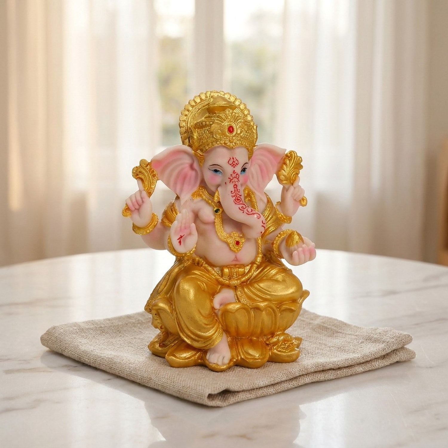 Statue de Ganesha en résine dorée sur surface marbre près d'une fenêtre avec voilage blanc