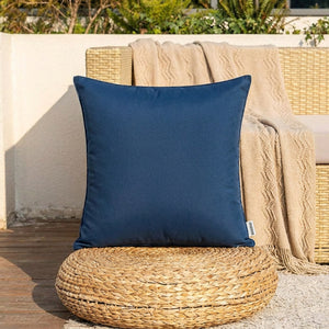 Housse de coussin extérieur bleu foncé posée sur un pouf en jonc tressé sur une terrasse