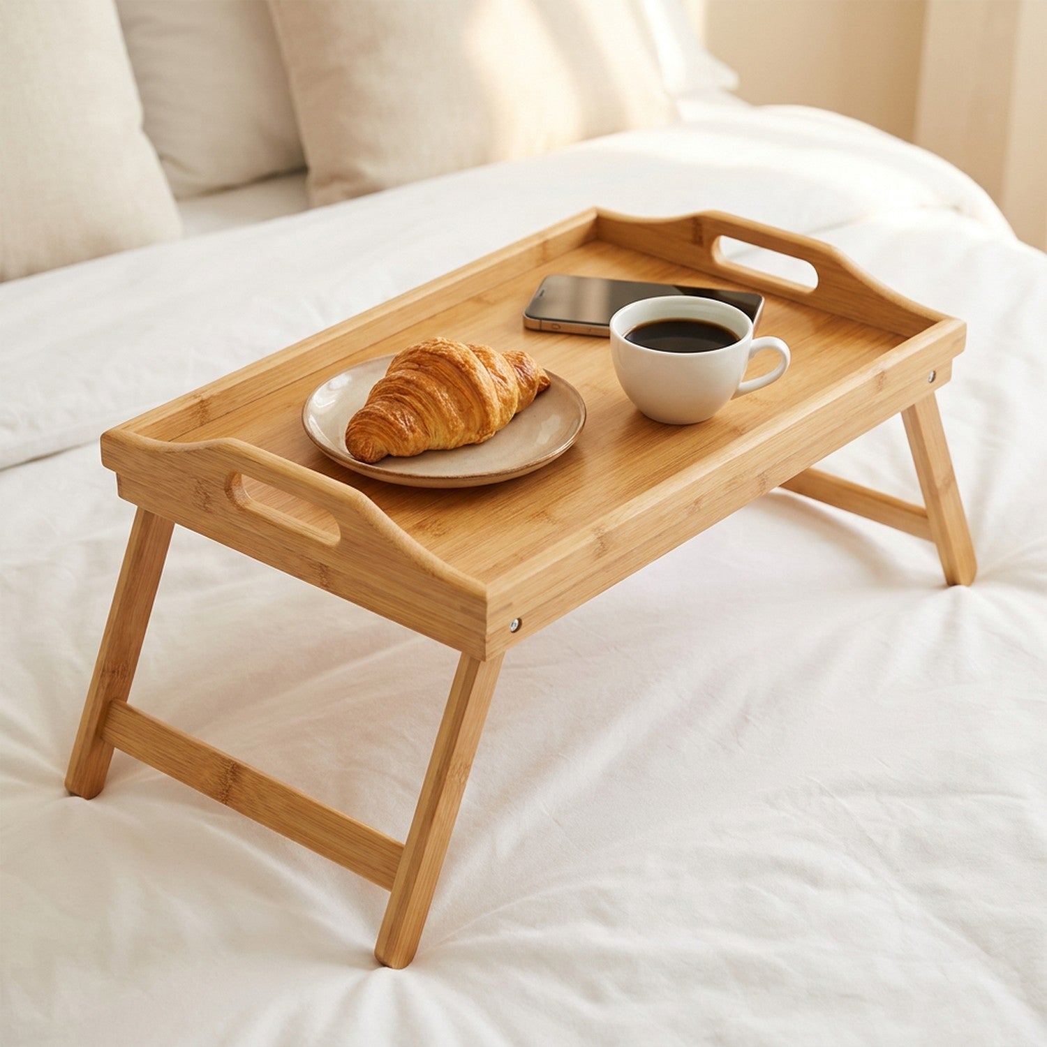 Plateau bambou sur lit avec un croissant, une tasse de café et un téléphone